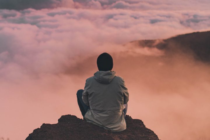 Man meditating on top of a mountain during a pink sunset.